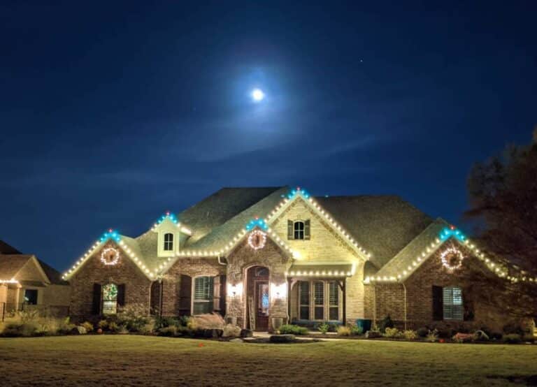 Christmas-decorated brick house illuminated at night under a bright moon.