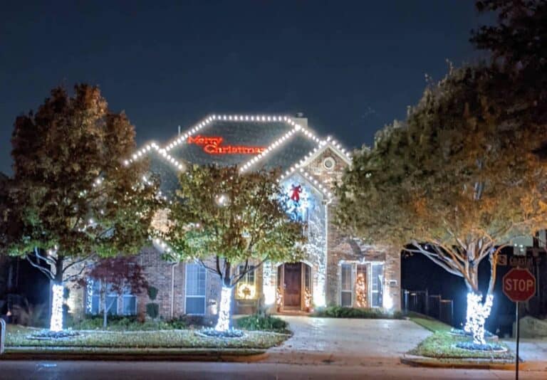 Festively decorated home with Christmas lights and a "Merry Christmas" sign at night.