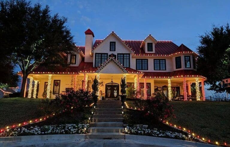 Elegant festive home adorned with vibrant holiday lights and lush landscaping at dusk.