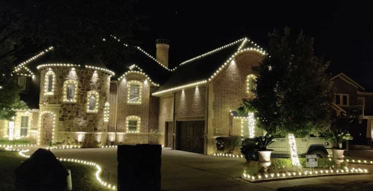 Festively illuminated brick house with string lights decorated for the holidays at night.