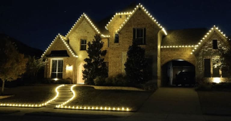 Beautifully illuminated brick home with festive lights outlining the roof and pathway at night.