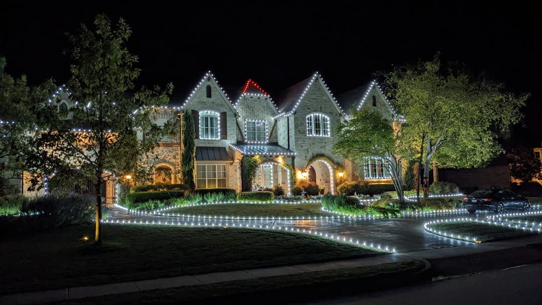 Elegant stone house illuminated with festive lights at night, surrounded by landscaped garden.