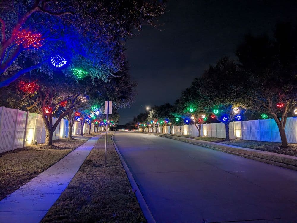 Decorated street with colorful holiday lights and trees at night.